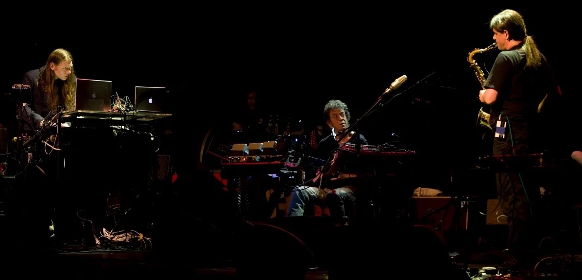 Lou Reed seated with his guitar, Metal Machine Trio on stage.