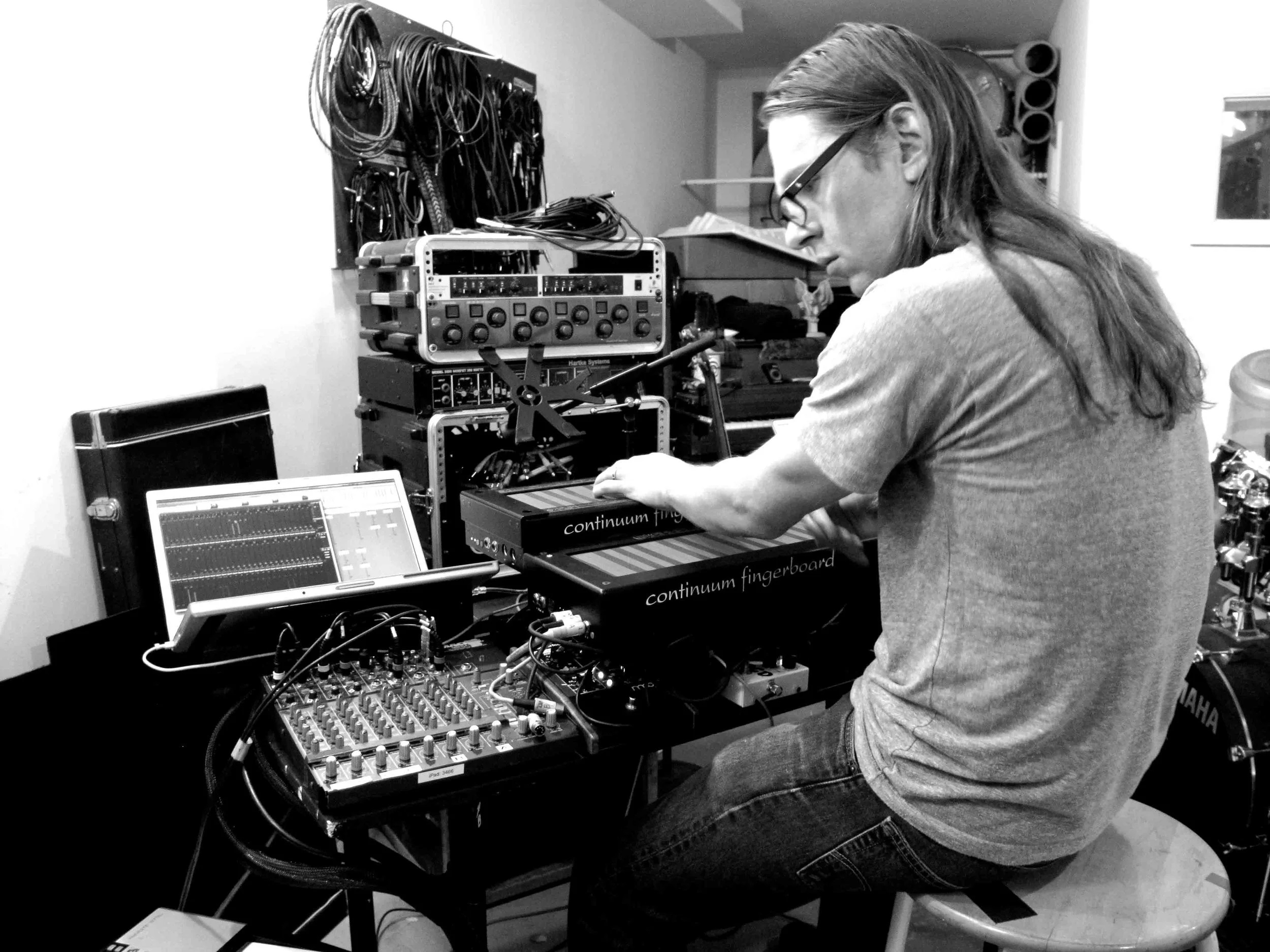 Sarth Calhoun seated at a Continuum Fingerboard with rack gear and a laptop.